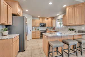 Kitchen featuring light stone counters, light brown cabinetry, appliances with stainless steel finishes, a kitchen bar, and recessed lighting