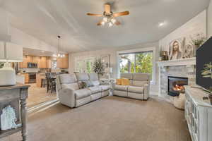 Living room featuring a ceiling fan, a stone fireplace, a chandelier, light carpet, and light tile patterned floors