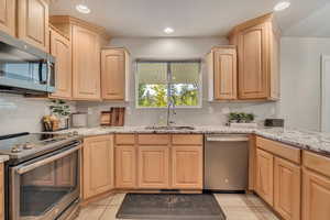 Kitchen with light brown cabinets, appliances with stainless steel finishes, backsplash, light stone countertops, and recessed lighting