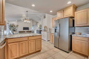 Kitchen with light brown cabinets, vaulted ceiling, stainless steel appliances, light stone countertops, and recessed lighting