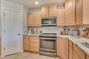 Kitchen with light brown cabinetry, appliances with stainless steel finishes, decorative backsplash, light stone counters, and recessed lighting