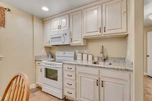 Kitchen with white appliances, light stone countertops, and recessed lighting