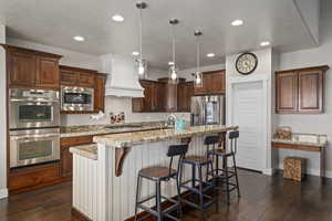 Kitchen with appliances with stainless steel finishes, pendant lighting, a breakfast bar area, a textured ceiling, and dark wood-style flooring
