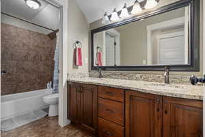 Bathroom featuring shower / bath combination with curtain, double vanity, a textured ceiling, and vaulted ceiling