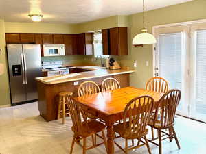 Kitchen featuring light countertops, light floors, white appliances, a peninsula, and hanging light fixtures
