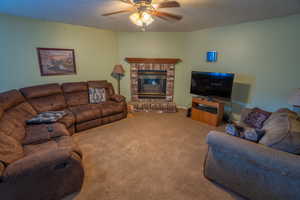 Carpeted living area featuring a fireplace and ceiling fan