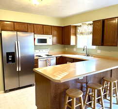 Kitchen with white appliances, a peninsula, light countertops, light floors, and a kitchen bar