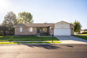 Ranch-style home featuring a front yard, brick siding, concrete driveway, and an attached garage