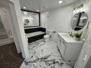 Full bath with a textured ceiling, a jetted tub, vanity, and recessed lighting