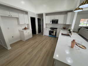 Kitchen featuring white cabinetry, light wood-style flooring, appliances with stainless steel finishes, light stone countertops, and high vaulted ceiling