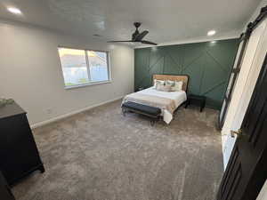 Bedroom featuring a barn door, carpet flooring, a textured ceiling, and a ceiling fan