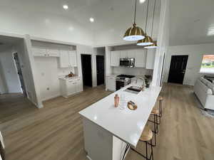 Kitchen with a breakfast bar area, open floor plan, white cabinets, stainless steel appliances, and hanging light fixtures