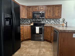 Kitchen with stainless steel appliances, brown cabinetry, decorative backsplash, dark countertops, and a peninsula