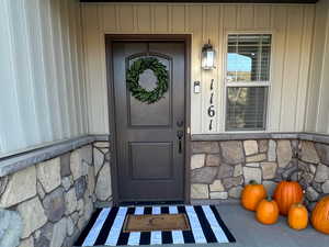 Entrance to property with stone siding, a porch, and board and batten siding