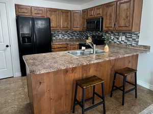 Kitchen featuring brown cabinets, backsplash, a breakfast bar area, black fridge with ice dispenser, and a textured ceiling