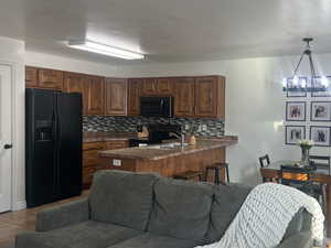 Kitchen with black appliances, dark countertops, decorative light fixtures, backsplash, and a peninsula