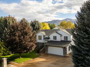 View of front of home featuring a mountain view, driveway, roof with shingles, an attached garage, and a front lawn