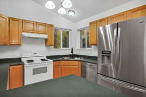 Kitchen featuring stainless steel appliances, dark countertops, under cabinet range hood, pendant lighting, and lofted ceiling