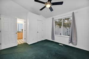 Primary bedroom with dark carpet, lofted ceiling, ceiling fan, and connected bathroom