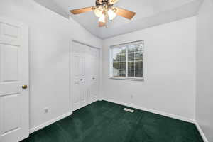 Upstairs bedroom featuring dark carpet, lofted ceiling, a closet, and ceiling fan