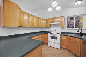 Kitchen featuring white electric range oven, hanging light fixtures, vaulted ceiling, light wood-style floors, and dark countertops
