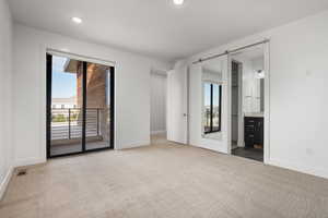 Unfurnished bedroom with access to exterior, carpet flooring, a barn door, recessed lighting, and ensuite bathroom