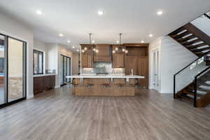 Kitchen with light wood-style flooring, custom exhaust hood, a spacious island, decorative light fixtures, and backsplash