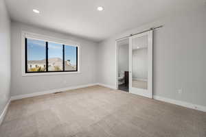 Unfurnished bedroom with a barn door, carpet floors, recessed lighting, and ensuite bath