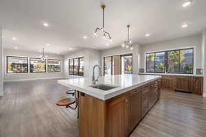 Kitchen with a chandelier, brown cabinetry, hanging light fixtures, a kitchen island with sink, and light wood-style flooring