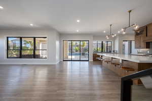 Kitchen with open floor plan, recessed lighting, hanging light fixtures, glass insert cabinets, and dark wood-type flooring