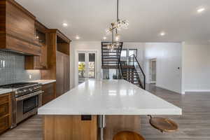 Kitchen featuring a kitchen island with sink, dark wood finished floors, stainless steel stove, pendant lighting, and backsplash