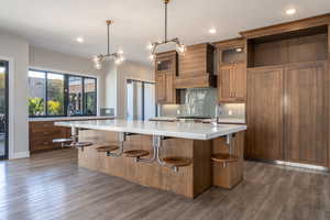 Kitchen featuring brown cabinets, backsplash, a breakfast bar area, hanging light fixtures, and dark wood-style floors
