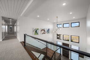 Hallway with an upstairs landing, recessed lighting, dark colored carpet, and a chandelier