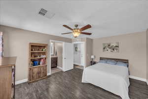 Bedroom with ceiling fan, dark wood-style flooring, and connected bathroom