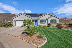 Ranch-style home featuring stucco siding, a front yard, driveway, roof mounted solar panels, and a mountain view