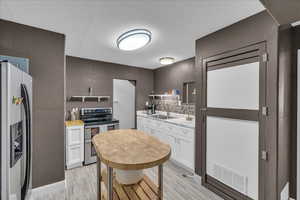 Kitchen featuring a textured wall, white cabinetry, light countertops, stainless steel appliances, and decorative backsplash