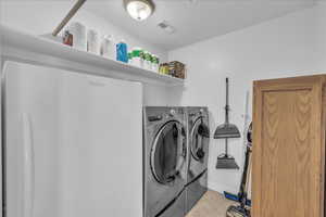 Washroom with washing machine and dryer and light tile patterned flooring