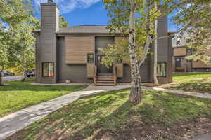 View of front facade with a front lawn, a chimney, entry steps, and a shingled roof