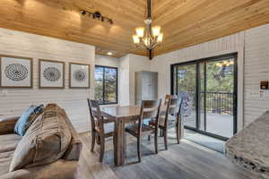 Dining room with wood walls, wood finished floors, wood ceiling, a chandelier, and track lighting