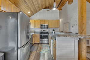 Kitchen featuring appliances with stainless steel finishes, light brown cabinetry, light wood-style flooring, wood ceiling, and a breakfast bar area