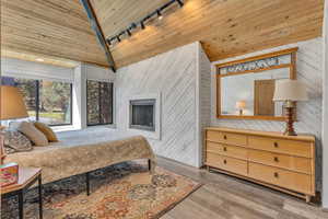 Bedroom featuring track lighting, wooden ceiling, wood walls, light wood finished floors, and a fireplace
