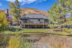 Back of house featuring a patio area, a lawn, a shingled roof, and a deck with water view
