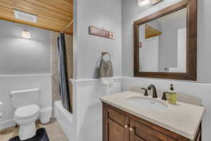 Full bath featuring wainscoting, wooden ceiling, shower / tub combo, vanity, and light tile patterned flooring
