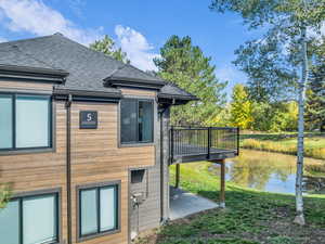 View of side of property featuring a deck with water view, roof with shingles, a lawn, and a patio