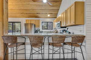 Kitchen featuring stainless steel appliances, a breakfast bar, wooden ceiling, vaulted ceiling, and wooden walls