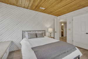 Bedroom with wood walls, light wood finished floors, and wooden ceiling