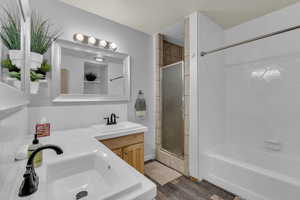 Bathroom with double vanity, dark wood-style floors, and enclosed tub / shower combo