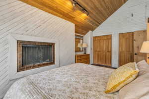 Bedroom with track lighting, wood walls, multiple closets, high vaulted ceiling, and wooden ceiling