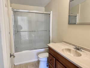 Full bath featuring enclosed tub / shower combo, vanity, a textured ceiling, a textured wall, and light tile patterned floors
