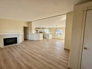 Living room with a tiled fireplace, a textured ceiling, light wood-style flooring, lofted ceiling, and a chandelier